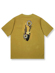 デザートイエローの背景にサボテンと野生の花の刺繍が施された「デザートフラワー」半袖Tシャツの正面ビュー。ゆったりとしたフィット感で、夏の日常着に理想的です。