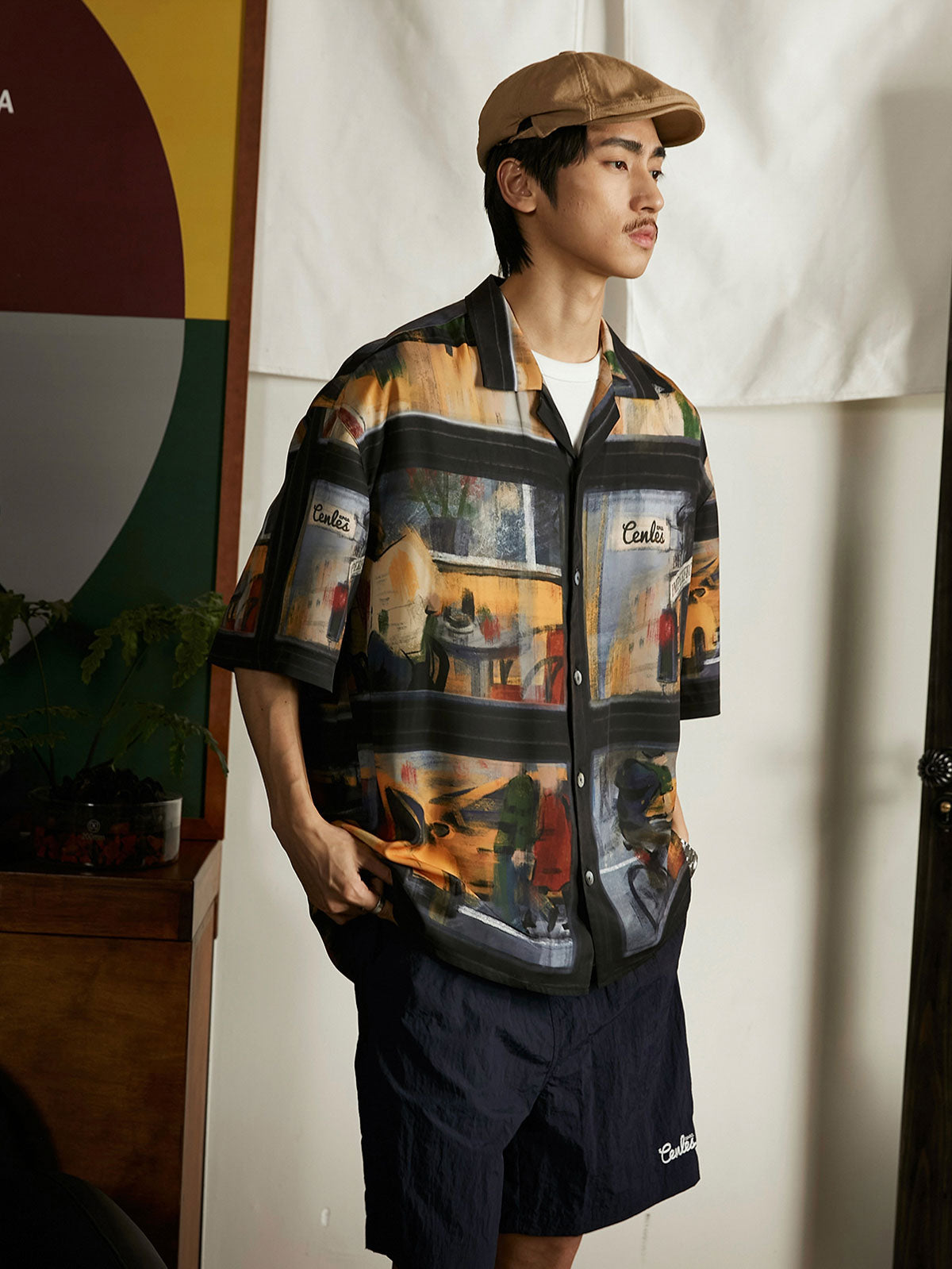 モデルが雨の日の街景油画風ハワイアンシャツを着用し、ジーンズとキャンバスシューズでコーディネート。ダークトーンのプリントがカジュアルながらもアートフルなスタイルを提供し、週末のリラックスしたアウトドアやカジュアルな街歩きに適しています。