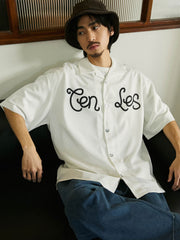 モデルが鮮やかなオレンジレッドのキューバカラー半袖シャツを着用し、ジーンズとキャンバスシューズでコーディネート。リラックスしたスタイルで週末の外出や休暇の旅行に最適なアウトフィットを演出しています。