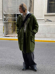 詳細画像: M-65改良型 厚手パーカーコート(ロング)のディテールクローズアップ画像。ウエストライン調整が可能なドローコードと、鍵やスマートフォンなどの収納に便利な多機能ポケットのデザインが映える。防風性を考慮した耐久性の高いコットン素材の質感が際立つ。
モデル画像: モデルが着用した**M-65改良型 厚手パーカーコート(ロング)**の全身コーディネートイメージ。ゆったりとしたシルエットとクラシックなミリタリースタイルを合わせ、ブーツやカジュアルシューズと相性抜群。アウトドアから日常使いまで幅広いシーンに対応する冬のスタイリング例。