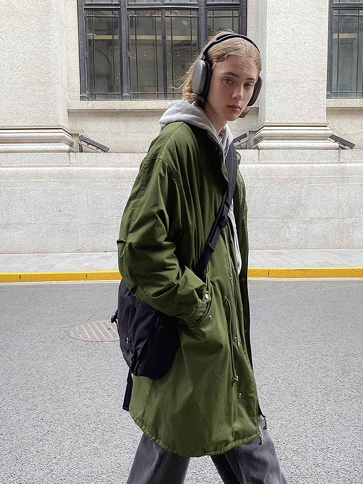 詳細画像: M-65改良型 厚手パーカーコート(ロング)のディテールクローズアップ画像。ウエストライン調整が可能なドローコードと、鍵やスマートフォンなどの収納に便利な多機能ポケットのデザインが映える。防風性を考慮した耐久性の高いコットン素材の質感が際立つ。
モデル画像: モデルが着用した**M-65改良型 厚手パーカーコート(ロング)**の全身コーディネートイメージ。ゆったりとしたシルエットとクラシックなミリタリースタイルを合わせ、ブーツやカジュアルシューズと相性抜群。アウトドアから日常使いまで幅広いシーンに対応する冬のスタイリング例。