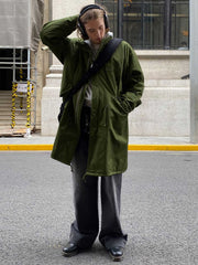 詳細画像: M-65改良型 厚手パーカーコート(ロング)のディテールクローズアップ画像。ウエストライン調整が可能なドローコードと、鍵やスマートフォンなどの収納に便利な多機能ポケットのデザインが映える。防風性を考慮した耐久性の高いコットン素材の質感が際立つ。
モデル画像: モデルが着用した**M-65改良型 厚手パーカーコート(ロング)**の全身コーディネートイメージ。ゆったりとしたシルエットとクラシックなミリタリースタイルを合わせ、ブーツやカジュアルシューズと相性抜群。アウトドアから日常使いまで幅広いシーンに対応する冬のスタイリング例。