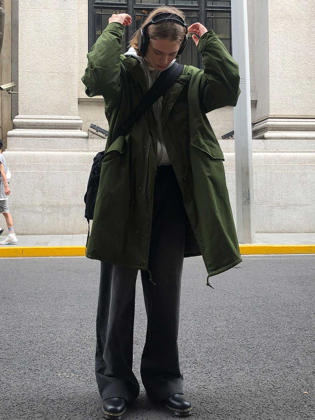 詳細画像: M-65改良型 厚手パーカーコート(ロング)のディテールクローズアップ画像。ウエストライン調整が可能なドローコードと、鍵やスマートフォンなどの収納に便利な多機能ポケットのデザインが映える。防風性を考慮した耐久性の高いコットン素材の質感が際立つ。
モデル画像: モデルが着用した**M-65改良型 厚手パーカーコート(ロング)**の全身コーディネートイメージ。ゆったりとしたシルエットとクラシックなミリタリースタイルを合わせ、ブーツやカジュアルシューズと相性抜群。アウトドアから日常使いまで幅広いシーンに対応する冬のスタイリング例。