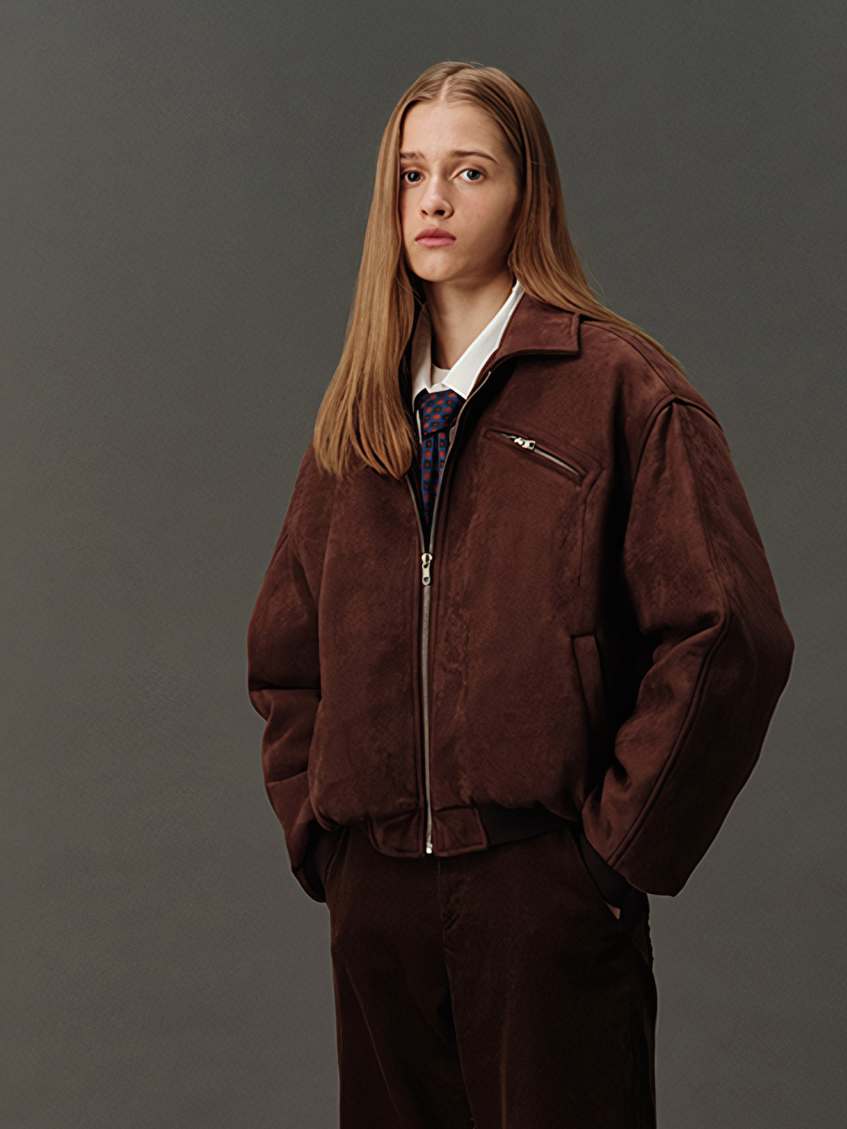 詳細画像: スエード調素材の滑らかな表面とキルティング加工による保温性を示すディテールクローズアップ画像。フラップカラーや多機能ポケットのデザインが際立つ。
モデル画像: スエード調ショート丈ダウンジャケットを着用したモデルのコーディネート例。レトロなブラウンカラーがヴィンテージ感を演出し、カジュアルパンツやワークパンツと相性抜群な秋冬スタイル。