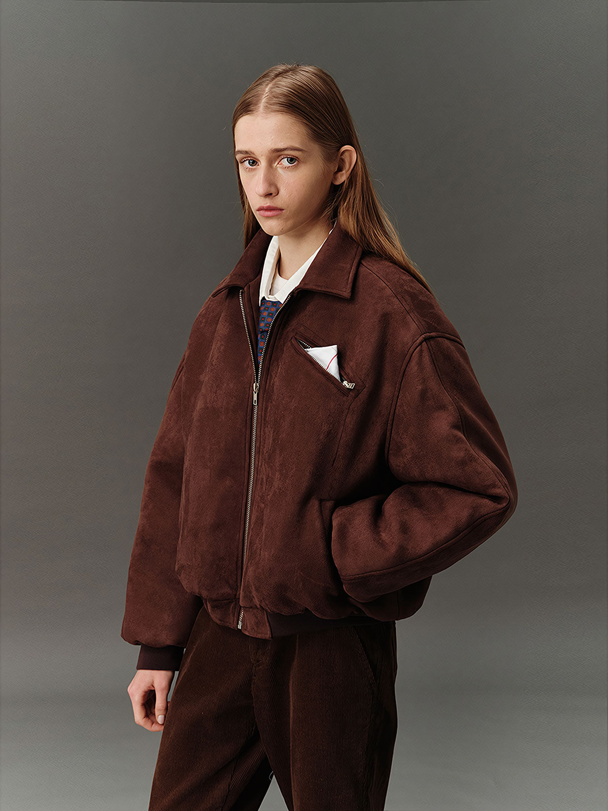 詳細画像: スエード調素材の滑らかな表面とキルティング加工による保温性を示すディテールクローズアップ画像。フラップカラーや多機能ポケットのデザインが際立つ。
モデル画像: スエード調ショート丈ダウンジャケットを着用したモデルのコーディネート例。レトロなブラウンカラーがヴィンテージ感を演出し、カジュアルパンツやワークパンツと相性抜群な秋冬スタイル。