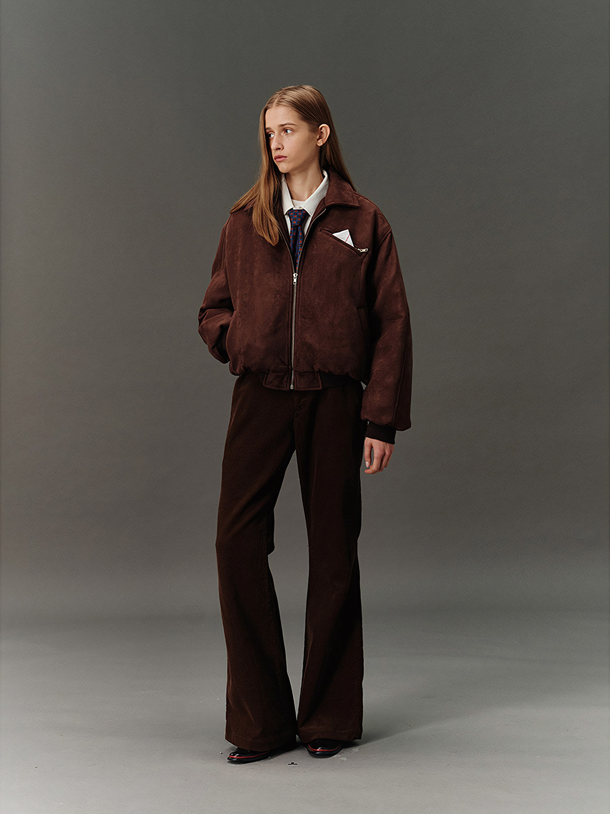 詳細画像: スエード調素材の滑らかな表面とキルティング加工による保温性を示すディテールクローズアップ画像。フラップカラーや多機能ポケットのデザインが際立つ。
モデル画像: スエード調ショート丈ダウンジャケットを着用したモデルのコーディネート例。レトロなブラウンカラーがヴィンテージ感を演出し、カジュアルパンツやワークパンツと相性抜群な秋冬スタイル。