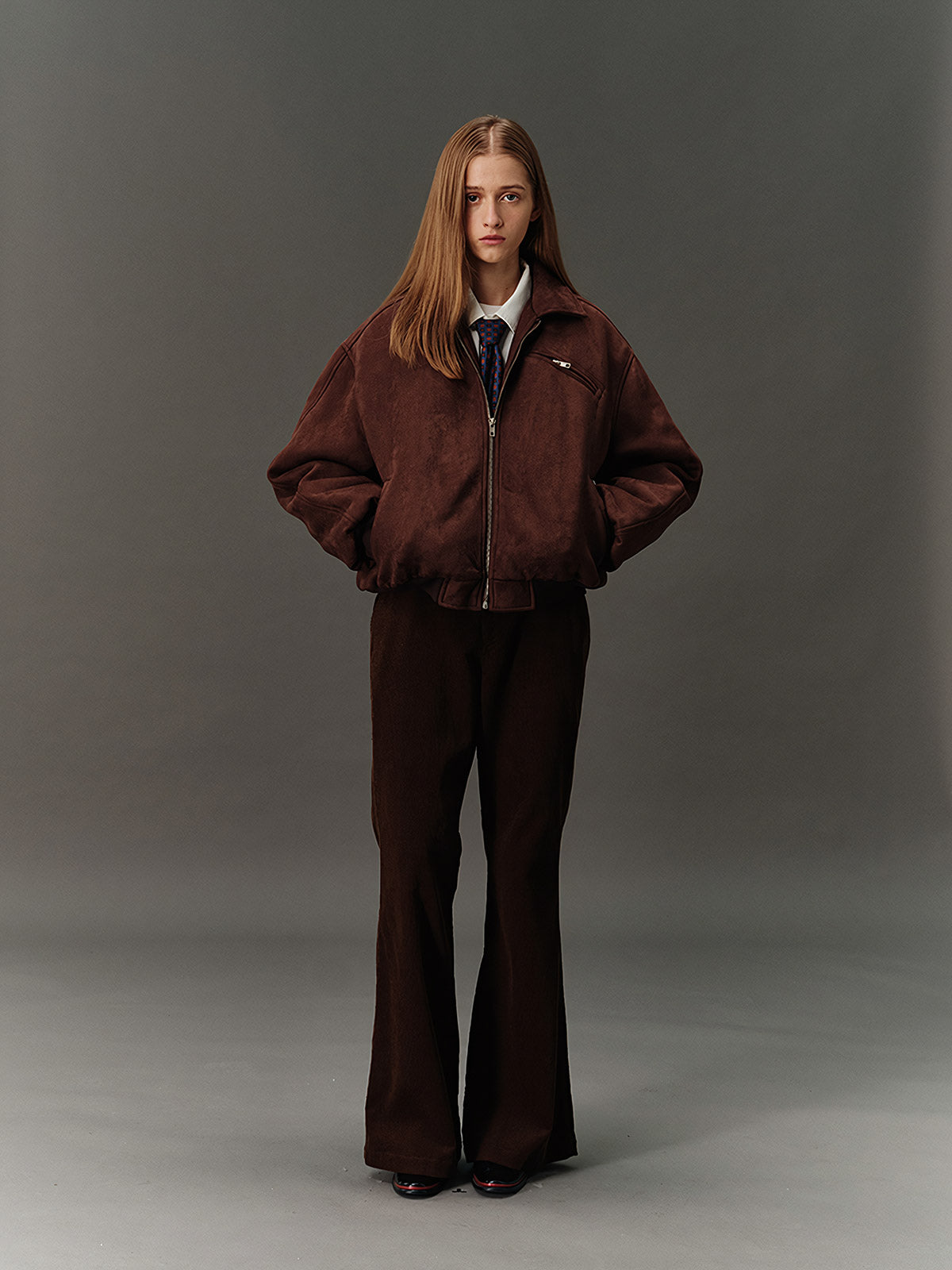 詳細画像: スエード調素材の滑らかな表面とキルティング加工による保温性を示すディテールクローズアップ画像。フラップカラーや多機能ポケットのデザインが際立つ。
モデル画像: スエード調ショート丈ダウンジャケットを着用したモデルのコーディネート例。レトロなブラウンカラーがヴィンテージ感を演出し、カジュアルパンツやワークパンツと相性抜群な秋冬スタイル。