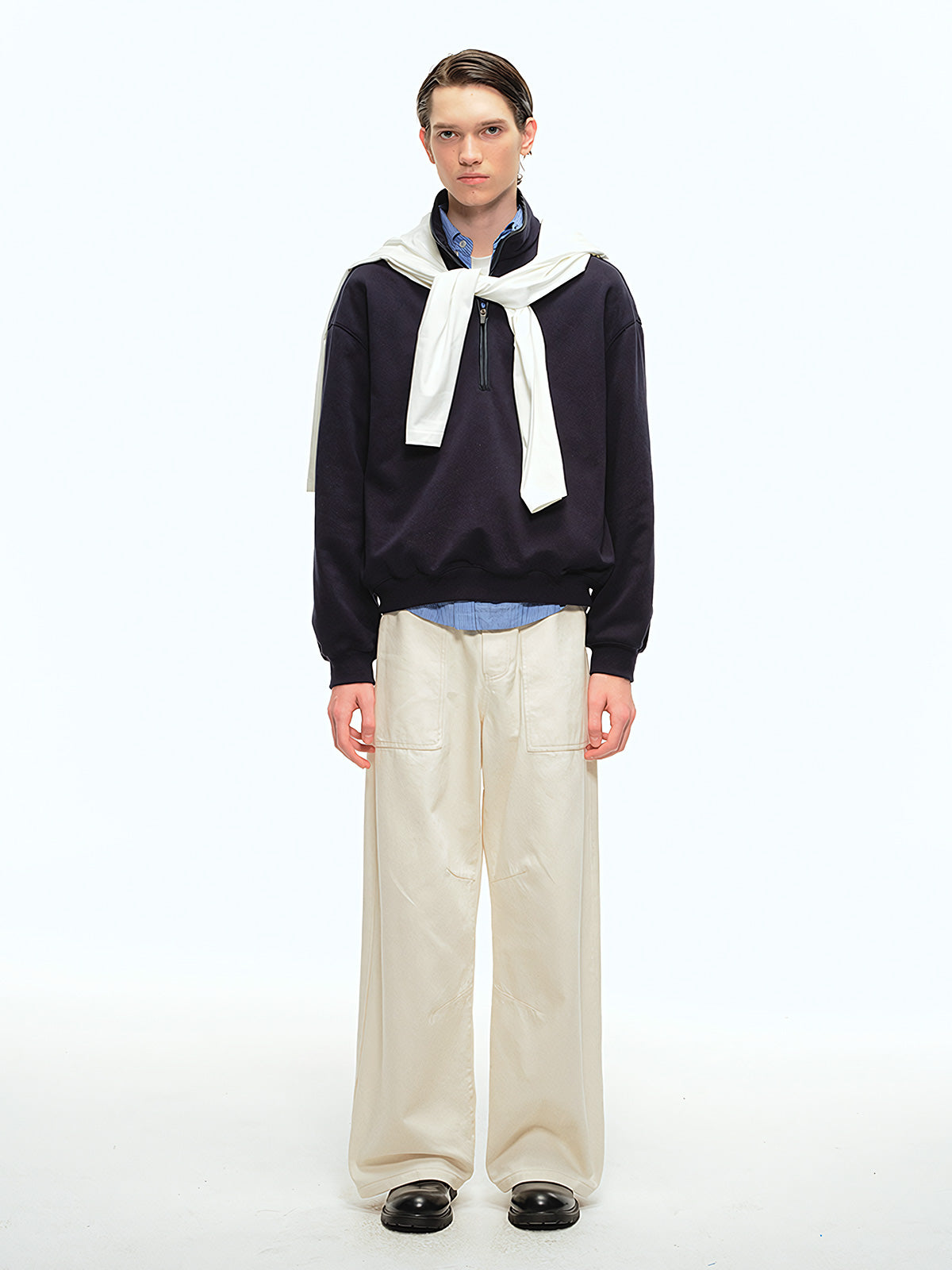 詳細画像: スタンドカラーとレザーパイピングのディテール特写。エコレザーの質感とハーフジップのディテールが強調され、デザイン性と実用性を高めています。
モデル画像: ハーフジップスウェットとカジュアルパンツを合わせたレトロで快適なスタイル。Boxyシルエットがリラックス感を与え、日常使いに最適なスタイリングを披露しています。