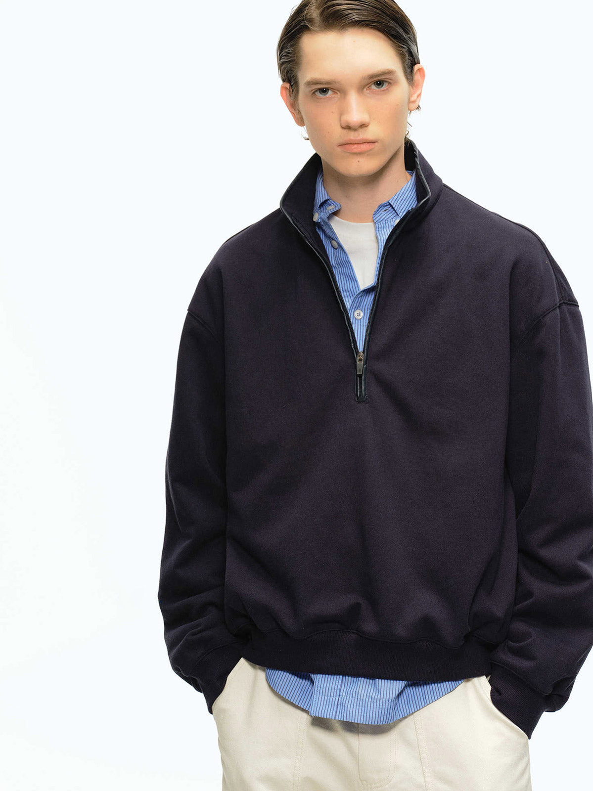 詳細画像: スタンドカラーとレザーパイピングのディテール特写。エコレザーの質感とハーフジップのディテールが強調され、デザイン性と実用性を高めています。
モデル画像: ハーフジップスウェットとカジュアルパンツを合わせたレトロで快適なスタイル。Boxyシルエットがリラックス感を与え、日常使いに最適なスタイリングを披露しています。