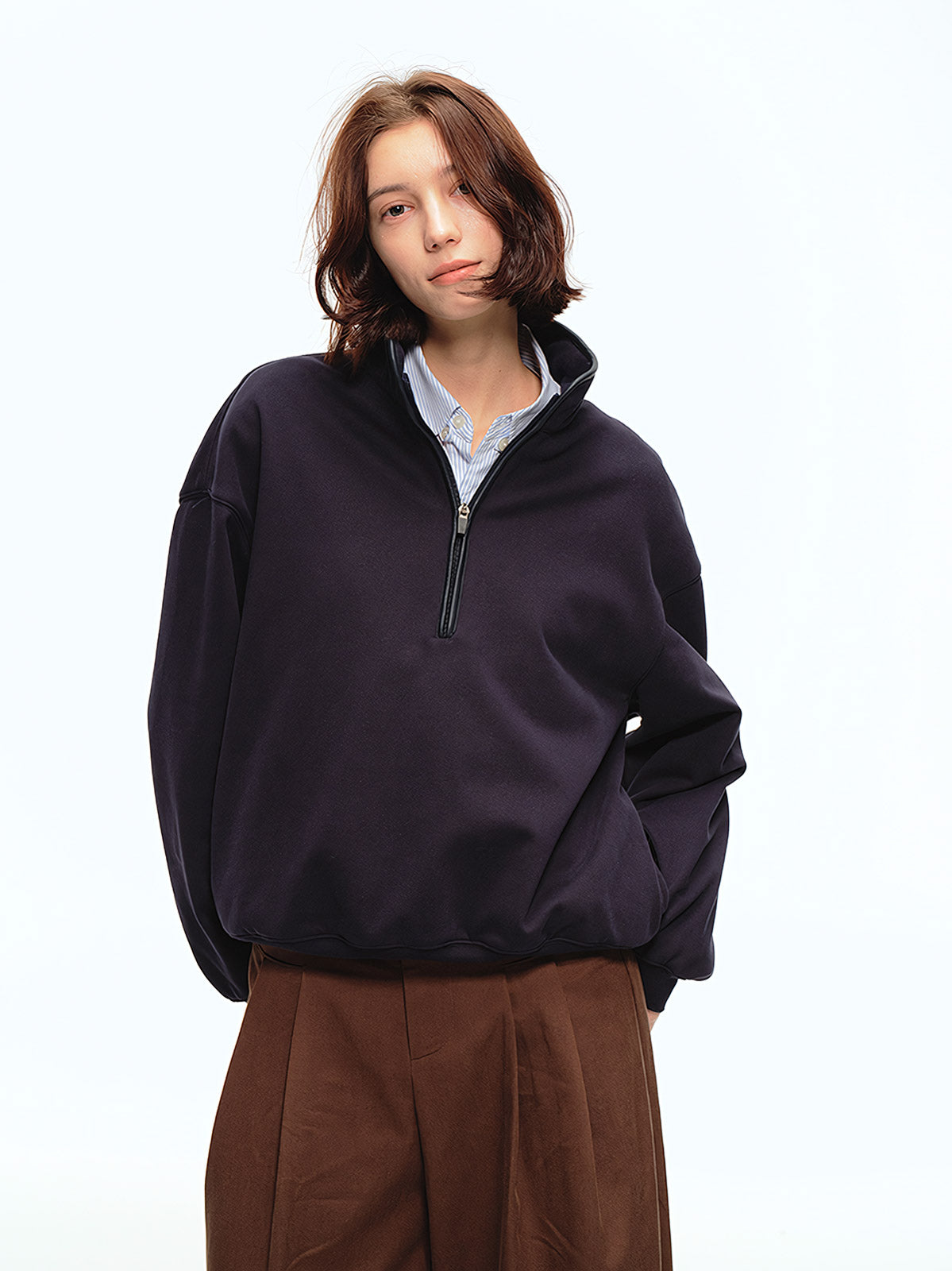 詳細画像: スタンドカラーとレザーパイピングのディテール特写。エコレザーの質感とハーフジップのディテールが強調され、デザイン性と実用性を高めています。
モデル画像: ハーフジップスウェットとカジュアルパンツを合わせたレトロで快適なスタイル。Boxyシルエットがリラックス感を与え、日常使いに最適なスタイリングを披露しています。