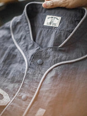 メテオライトグレーのベースボールシャツ、胸元に「GRIT PERSEVERANCE」フェルトパッチが施されている