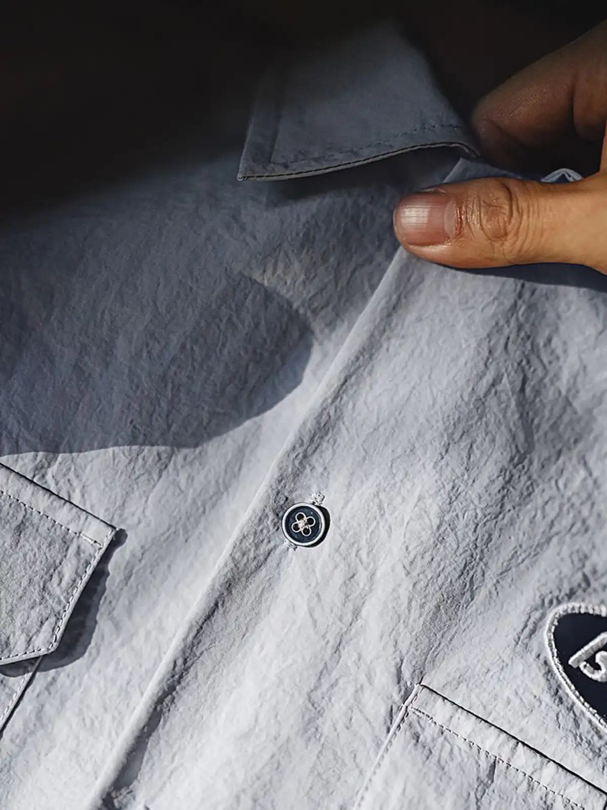 薄手のナイロン生地と2つの胸ポケットが特徴の半袖シャツ正面全体。肩のロゴ刺繍や控えめなスタイリングがわかる