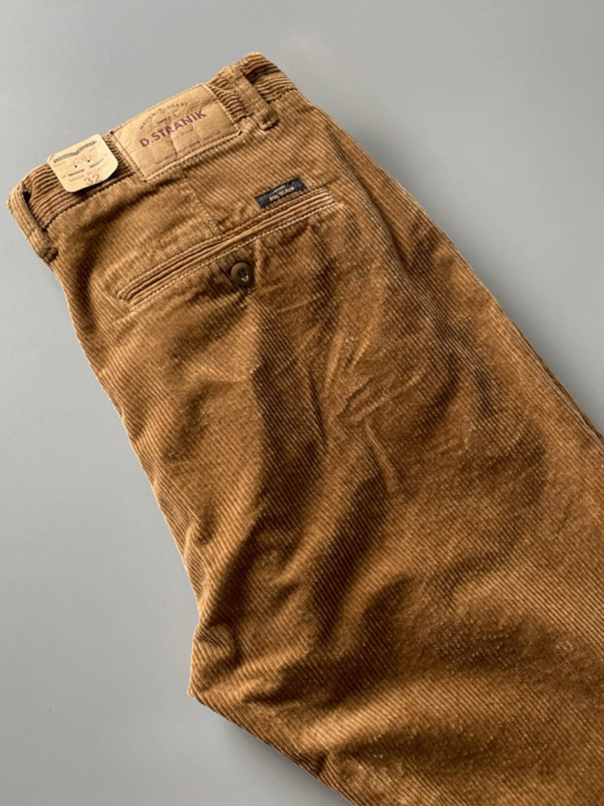 製品画像
高密度の14畝コーデュロイ素材を使用したストレートカーゴパンツ。クラシックなストレートシルエットとウォッシュ加工によるヴィンテージ感が特徴で、鉱山作業着の伝統を受け継ぐデザインが際立つ
詳細画像
バックポケットに施された二重補強ディテールとウエスト内側の丁寧なパイピング仕上げが、機能性とクラシックな仕立ての美学を象徴。コーデュロイの均一な畝立ちが繊細な質感を強調