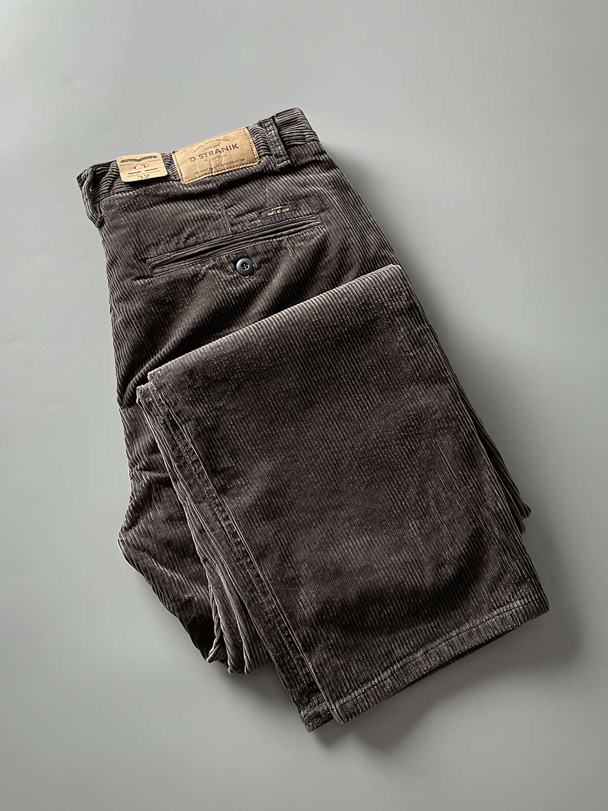 製品画像
高密度の14畝コーデュロイ素材を使用したストレートカーゴパンツ。クラシックなストレートシルエットとウォッシュ加工によるヴィンテージ感が特徴で、鉱山作業着の伝統を受け継ぐデザインが際立つ
詳細画像
バックポケットに施された二重補強ディテールとウエスト内側の丁寧なパイピング仕上げが、機能性とクラシックな仕立ての美学を象徴。コーデュロイの均一な畝立ちが繊細な質感を強調