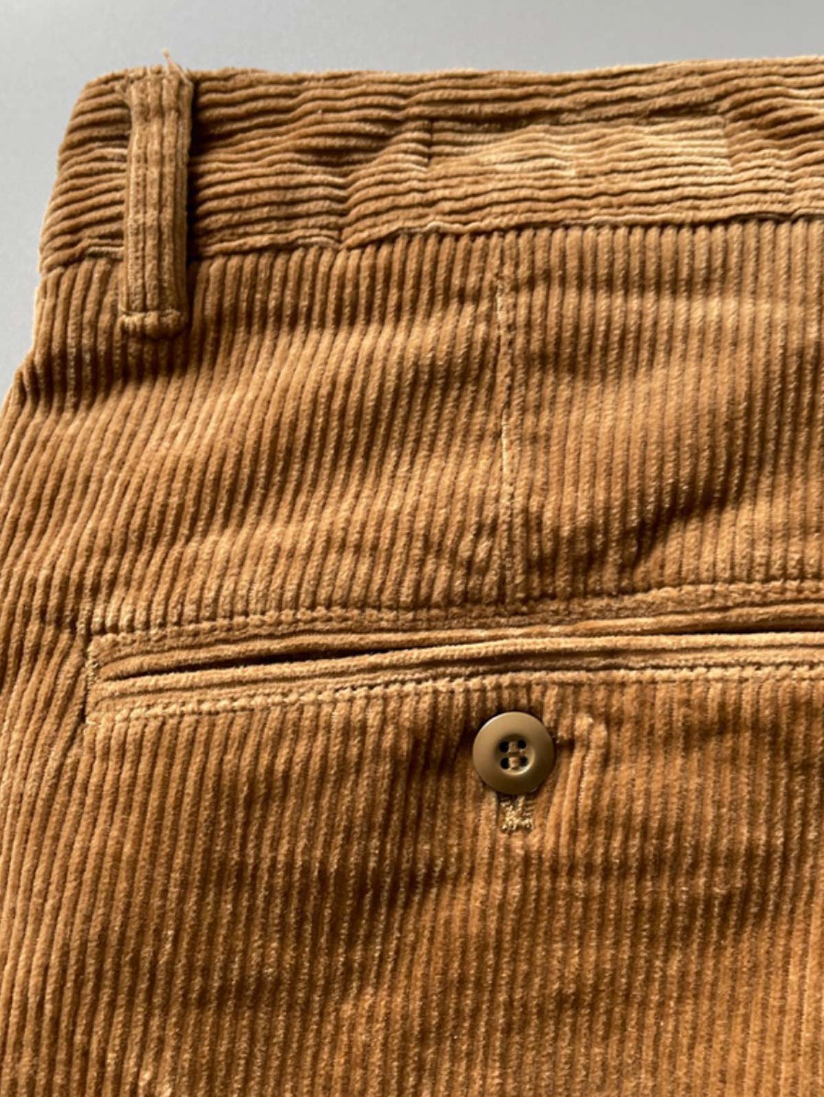 製品画像
高密度の14畝コーデュロイ素材を使用したストレートカーゴパンツ。クラシックなストレートシルエットとウォッシュ加工によるヴィンテージ感が特徴で、鉱山作業着の伝統を受け継ぐデザインが際立つ
詳細画像
バックポケットに施された二重補強ディテールとウエスト内側の丁寧なパイピング仕上げが、機能性とクラシックな仕立ての美学を象徴。コーデュロイの均一な畝立ちが繊細な質感を強調