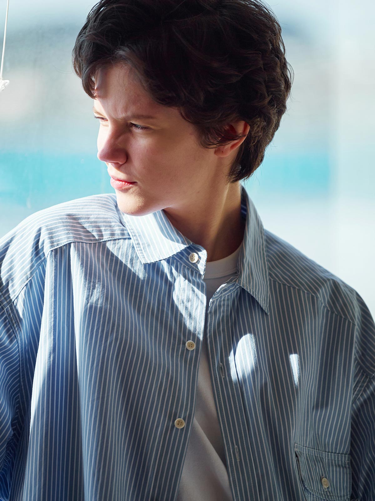 詳細画像: 胸ポケットとストライプ柄のディテール特写。精緻な織り目と均一なデザインが、ヴィンテージ感を引き立てつつ、現代的なカジュアルさも加えています。クロスステッチでの仕上げが、デザインの深みと耐久性を強調。
モデル画像: レトロストライプシャツとルーズパンツを合わせたカジュアルヴィンテージスタイル。ドロップショルダーとやや短めの丈が、現代的なカジュアル感を加え、快適で動きやすいシルエットを演出します。