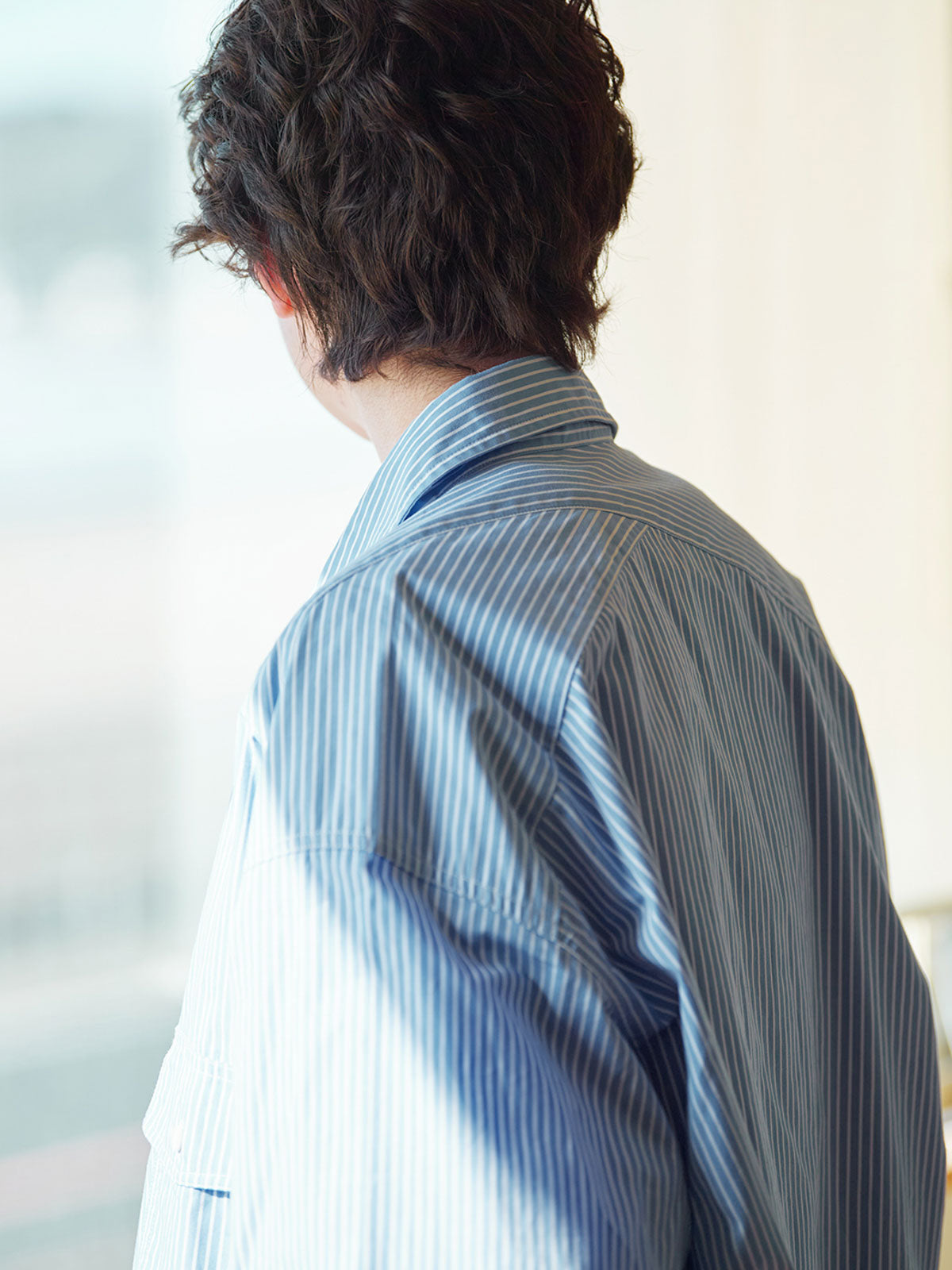 詳細画像: 胸ポケットとストライプ柄のディテール特写。精緻な織り目と均一なデザインが、ヴィンテージ感を引き立てつつ、現代的なカジュアルさも加えています。クロスステッチでの仕上げが、デザインの深みと耐久性を強調。
モデル画像: レトロストライプシャツとルーズパンツを合わせたカジュアルヴィンテージスタイル。ドロップショルダーとやや短めの丈が、現代的なカジュアル感を加え、快適で動きやすいシルエットを演出します。