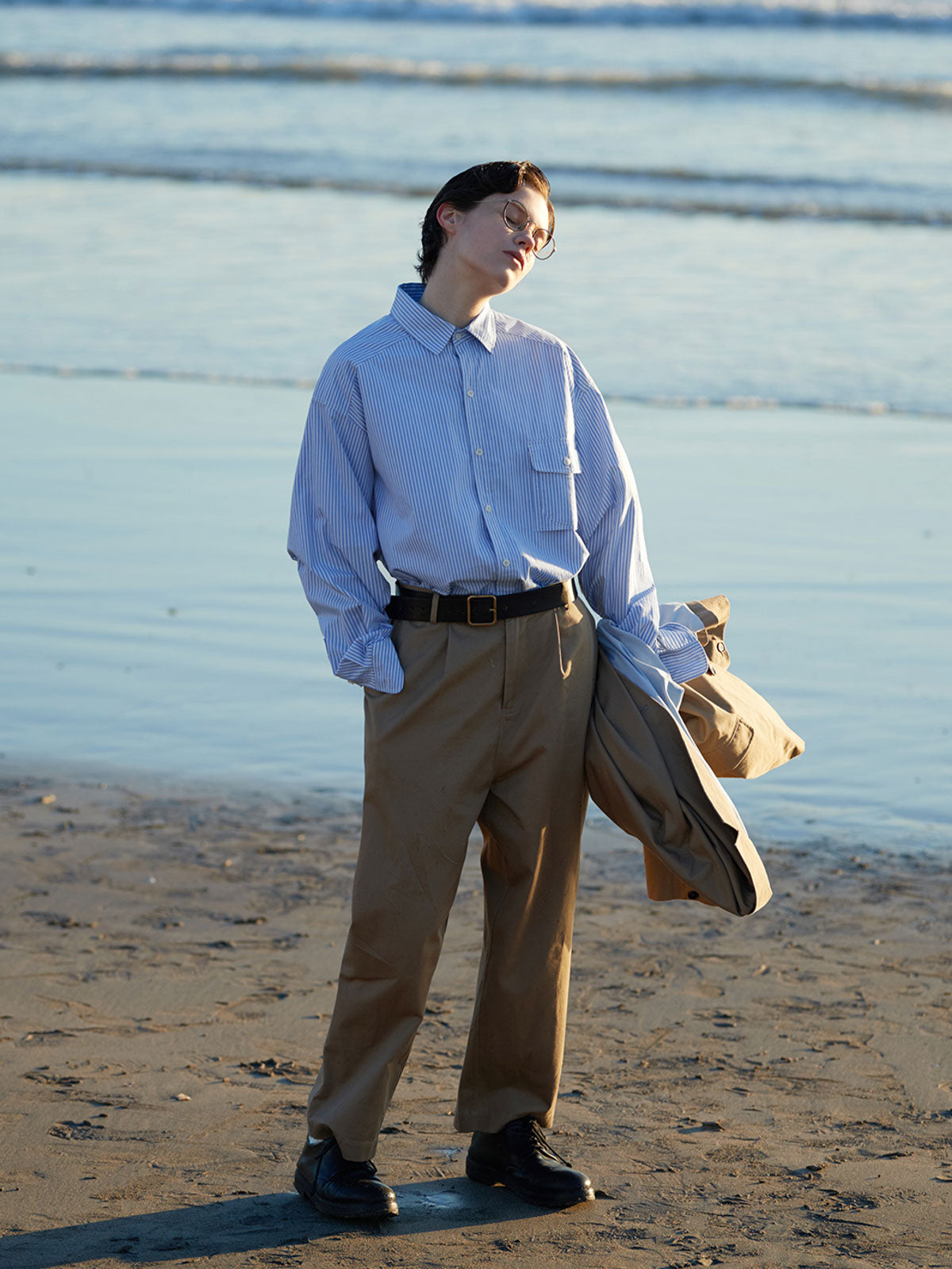 詳細画像: 胸ポケットとストライプ柄のディテール特写。精緻な織り目と均一なデザインが、ヴィンテージ感を引き立てつつ、現代的なカジュアルさも加えています。クロスステッチでの仕上げが、デザインの深みと耐久性を強調。
モデル画像: レトロストライプシャツとルーズパンツを合わせたカジュアルヴィンテージスタイル。ドロップショルダーとやや短めの丈が、現代的なカジュアル感を加え、快適で動きやすいシルエットを演出します。