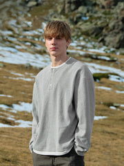 詳細画像: ワッフル生地のテクスチャーとレイヤードデザインの特写。独自の質感とディテールが着こなしに深みを加え、シンプルでありながらもデザイン性が光る。
モデル画像: ヘンリーネック長袖Tシャツを着用したカジュアルなレイヤードスタイルを披露するモデル。ゆったりとしたシルエットと快適さを兼ね備え、スタイリッシュな着こなしを実現。