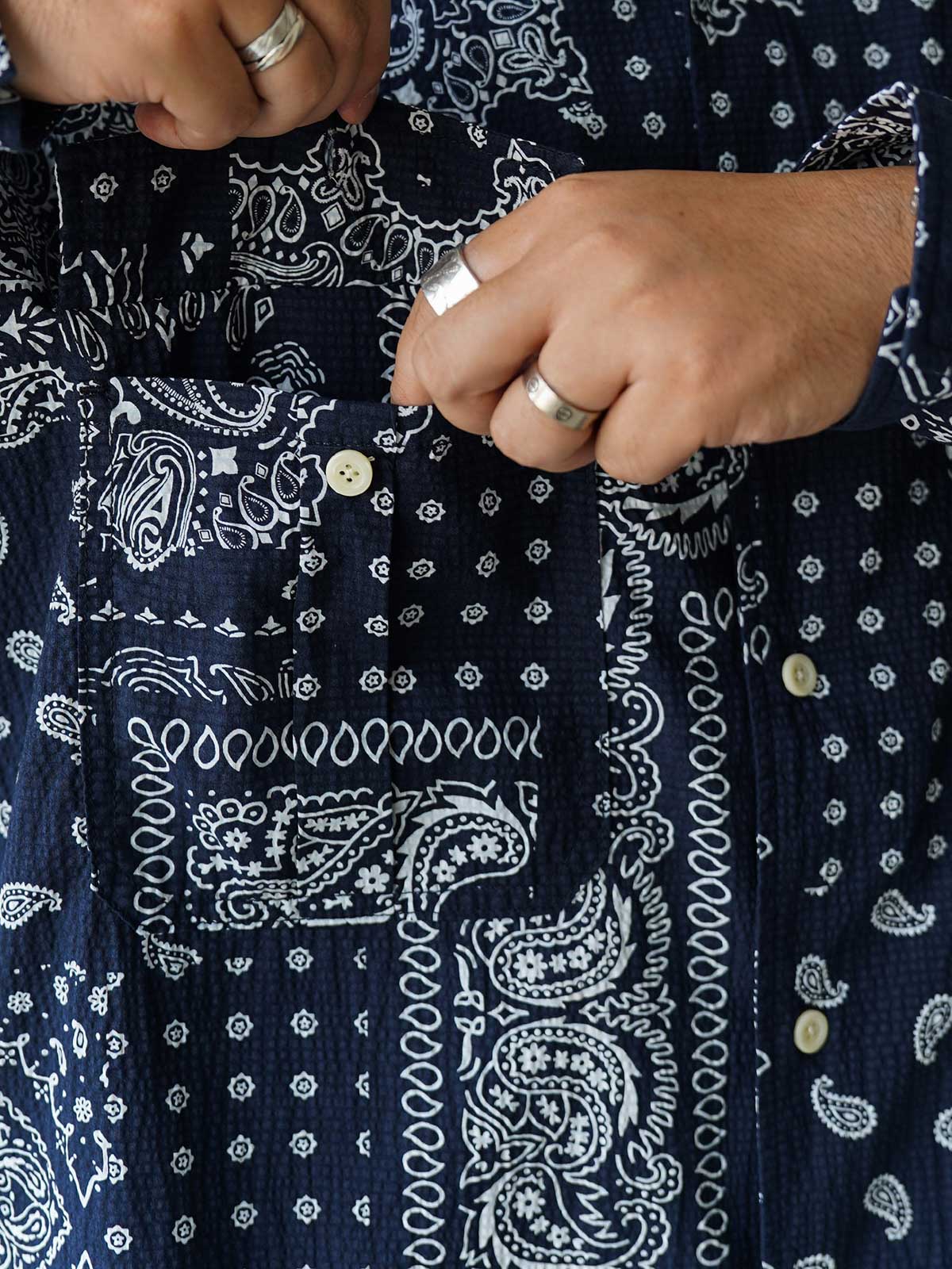 製品画像
ペイズリー柄シアサッカーシャツの正面デザイン。アメリカンバンダナ文化を反映した不規則なプリントパターンと、軽量で通気性の高いシアサッカー生地が特徴
詳細画像
3つのポケットと独特なシワ感を持つシアサッカー生地のディテール。18針/3cmの高密度縫製工法による精密な仕上がりが際立つ