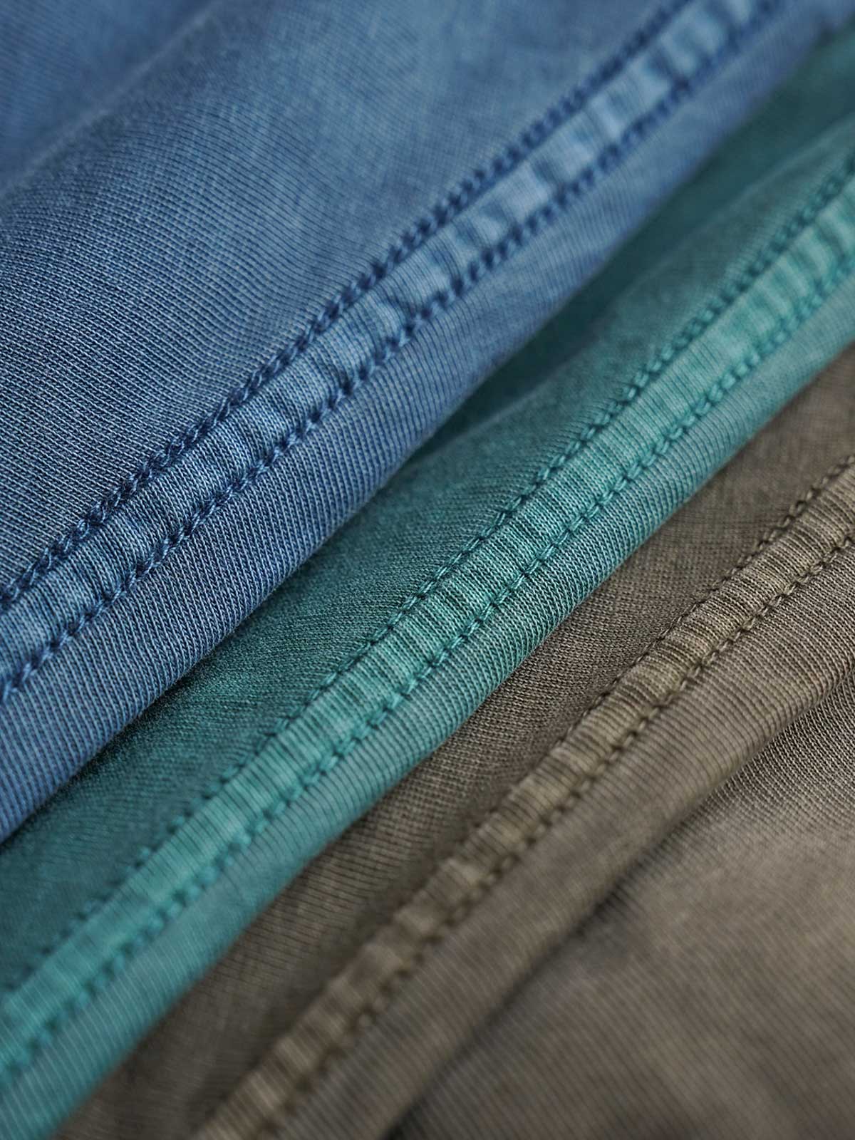 製品画像
ヴィンテージ蝋染めスウェットシャツ正面デザイン。グレイッシュグリーンやデニムブルーなどの植物染料で仕上げた深みのある色合いと、ルーズフィットのシルエットが特徴。日本伝統の蝋染め技法によるユニークな色彩表現が際立つ一着
詳細画像
ネックライン周辺の精密な3cmあたり18針ステッチと、蝋染め加工で生まれる独特な色彩の層次感を特写。二重構造の肩テープとサイドステッチのディテールが、耐久性と快適な着心地を提供する仕上がり