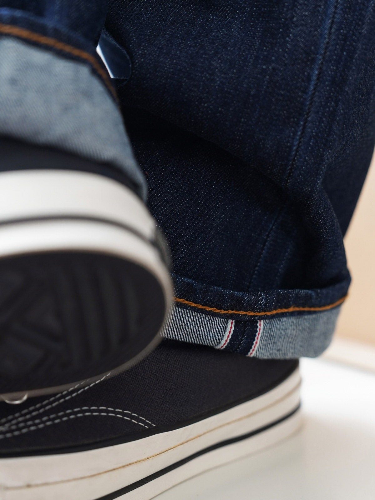 詳細画像
「赤耳セルビッジ、インディゴ染め鹿革パッチ、月桂冠モチーフのドーナツボタン、カスタムYKKジッパーなど、クラシックで高級感のあるディテールのクローズアップ。」
モデル画像
「モデルがワークジャケットと組み合わせて着用した赤耳デニムパンツ。ヴィンテージ感とややルーズフィットのシルエットが特徴のアメカジコーディネート。」