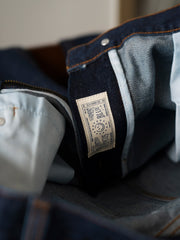 製品画像
「14OZ赤耳デニムパンツ全体イメージ。旧式織機で織られたクラシックな狭幅赤耳デニム生地とインディゴ染めの高品質な仕上がりが特徴。」
詳細画像
「赤耳セルビッジ、インディゴ染め鹿革パッチ、月桂冠モチーフのドーナツボタン、カスタムYKKジッパーなど、クラシックで高級感のあるディテールのクローズアップ。」