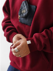 詳細画像
「伝統的なカンガルーポケットと厚手リブ仕様の裾、袖口のディテールクローズアップ。345gの裏起毛生地で保温性と耐久性を実現。」
モデル画像
「モデルがデニムパンツと合わせて着用したアンゴラレッドの裏起毛パーカー。90年代ストリートカルチャーを彷彿とさせるルーズフィットシルエットで冬のスタイリングを演出。」