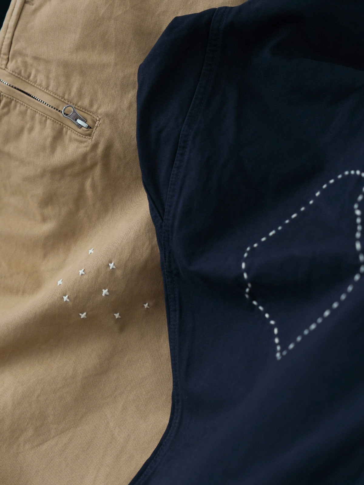 製品画像
「刺し子の伝統工芸を取り入れたハンド刺し子テーパードパンツ全体イメージ。高密度磨毛コットンツイル生地を使用し、快適さと耐久性を兼ね備えたデザイン。」
詳細画像
「非対称の刺し子刺繍ディテールと大容量の弧形ポケットをクローズアップ。膝部分の左右異なる刺繍パターンが立体感を強調。」