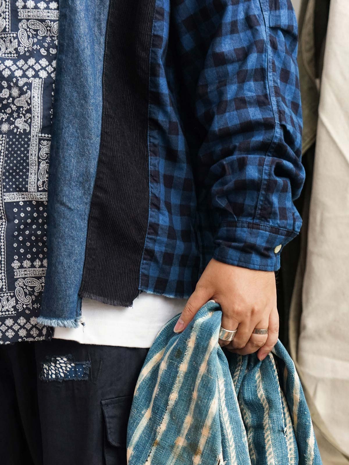 詳細画像
「REMAKE パッチワーク アシンメトリーヘム 長袖シャツの素材ディテール特写。藍染め織りのチェック柄やペイズリー柄、デニム、コーデュロイなど6種類の異素材を組み合わせたパッチワークと、動きのあるアシンメトリーヘムのクローズアップ。袖部分には調節可能なタブも配置。」
モデル画像
「REMAKE パッチワーク アシンメトリーヘム 長袖シャツを着用したモデルが、デニムパンツと合わせたリラックス感のあるレトロなカジュアルスタイルを披露。ルーズフィットとドロップショルダーのカッティングがトレンド感を強調。」