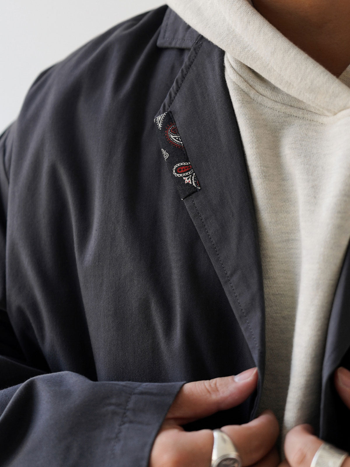 詳細画像
「不規則に配置されたペイズリー柄パッチと高密度ヘリンボーン裏地のディテールクローズアップ。機能性とファッション性を融合したデザイン。」
モデル画像
「モデルがヴィンテージ ペイズリー柄パッチルーズフィット テーラードジャケットをデニムパンツとスニーカーに合わせたリラックスしたカジュアルコーディネート。」