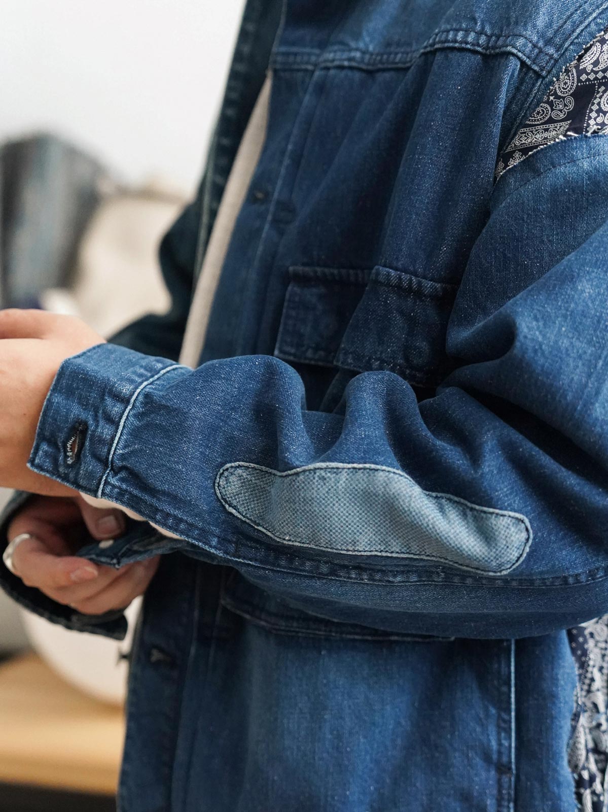 詳細画像
「デコンストラクション パッチワーク ペイズリー柄 デニムジャケットのディテール特写。袖口や裾に施されたペイズリー柄パッチワークのクラフトマンシップや、意図的にずらしたボタンデザインが、ヴィンテージ感と個性を際立たせる。左右非対称の再構築デザインが視覚的なユニークさを演出。」
モデル画像
「デコンストラクション パッチワーク ペイズリー柄 デニムジャケットを着用したモデルが、ワークパンツと組み合わせたレトロなヴィンテージスタイルを披露。オーバーサイズシルエットで自由な着こなしが楽しめるトレンド感あふれるコーディネート。」