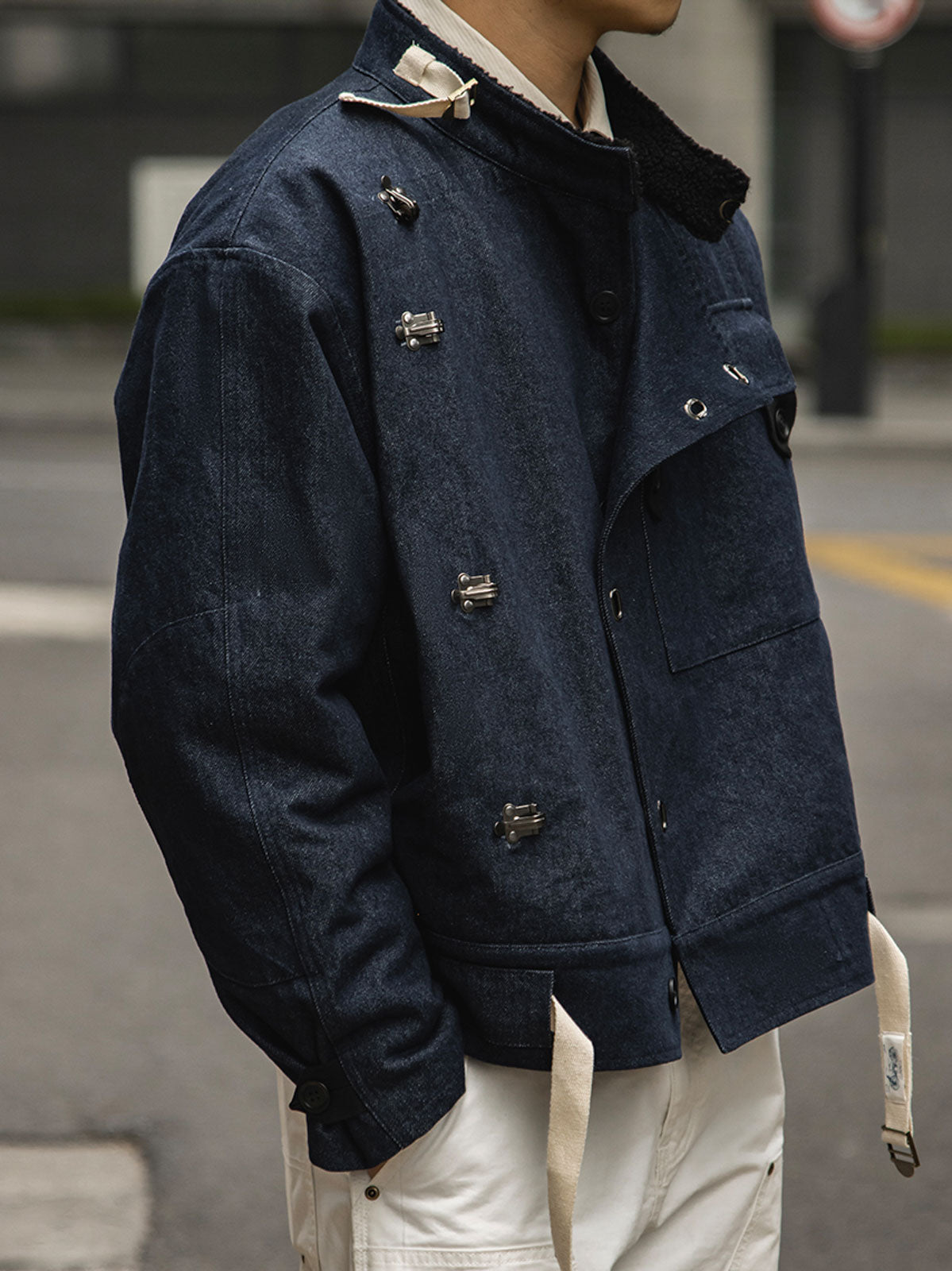 詳細画像
デッキフックとスウェードラベルのディテールクローズアップ。海軍スタイルのボタンとレトロなデザインがミリタリー感を際立たせる。
モデル画像
モデルが着用したレトロなバイカージャケットの冬のスタイル展示。デニムとワークブーツとの相性が抜群で、硬派な冬のコーディネートが完成。