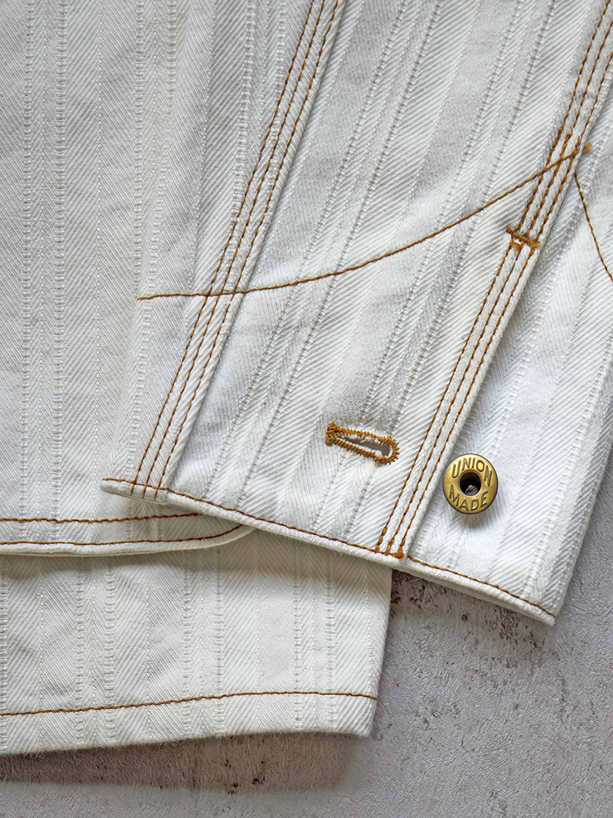 製品画像:
アイボリーヘリンボーン織りのワークジャケット全体画像。クラシックで高級感あるデザイン。
詳細画像:
コントラストステッチのディテール。精巧な縫製がジャケットの魅力を引き立てます。