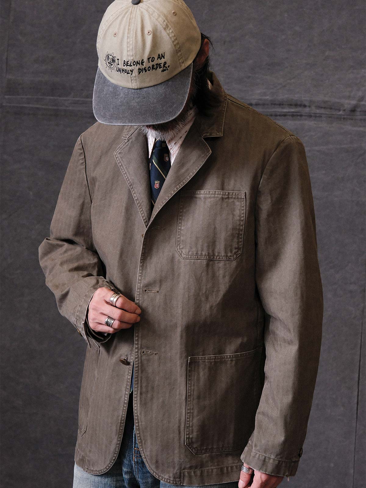 詳細画像: ウォッシュ加工されたヘリンボーン柄の生地とヴィンテージメタルボタンのディテール
モデル画像: ゆるやかなフィットでスタイリッシュなヴィンテージウォッシュジャケットの着用イメージ