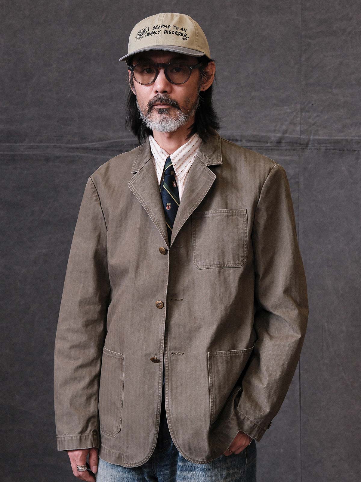 詳細画像: ウォッシュ加工されたヘリンボーン柄の生地とヴィンテージメタルボタンのディテール
モデル画像: ゆるやかなフィットでスタイリッシュなヴィンテージウォッシュジャケットの着用イメージ