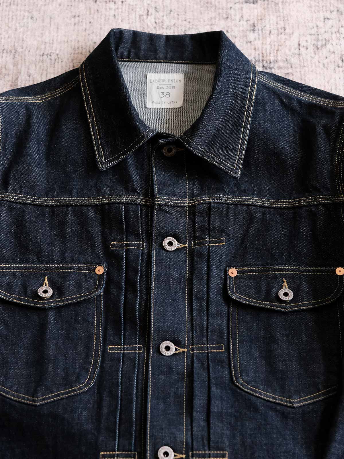 製品画像:
15.5oz生赤耳デニムジャケット全体展示。日本製の赤耳デニム素材を使用したクラシックなデザインで、レトロ感が溢れ、着心地も抜群。
詳細画像:
赤耳部分のディテールと金属ボタンのクローズアップ。伝統的な赤耳処理とクラシックな金属ボタンがヴィンテージスタイルを際立たせます。