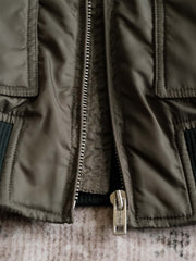 製品画像:
CWU-45Pフライトジャケット全体展示。高密度ナイロン素材と厚手のキルティング綿を使用し、ミリタリースタイルと快適性を兼ね備えたクラシックなデザイン。
詳細画像:
TALONメタルジッパーとマジックテープエンブレムのディテール。レトロ感あふれるエンブレムとジッパーが、クラシックなフライトジャケットの魅力を引き立てます。