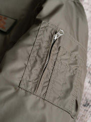 製品画像:
CWU-45Pフライトジャケット全体展示。高密度ナイロン素材と厚手のキルティング綿を使用し、ミリタリースタイルと快適性を兼ね備えたクラシックなデザイン。
詳細画像:
TALONメタルジッパーとマジックテープエンブレムのディテール。レトロ感あふれるエンブレムとジッパーが、クラシックなフライトジャケットの魅力を引き立てます。