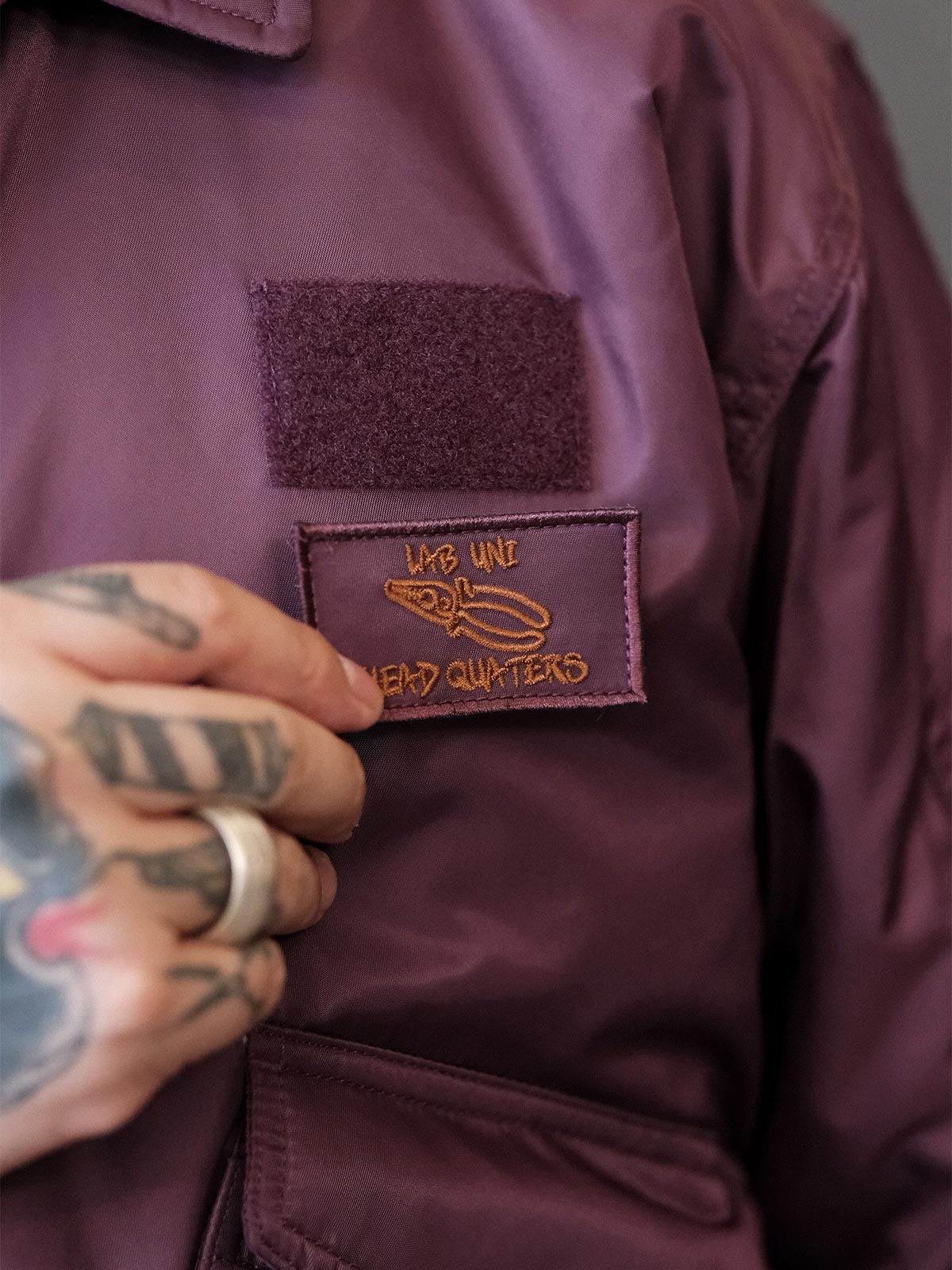 製品画像:
CWU-45Pフライトジャケットの全体展示。高密度ナイロン外層と厚手のキルティング綿を使用した、保温性と防風性に優れたクラシックなフライトジャケットの全体像。
詳細画像:
TALONメタルジッパーとマジックテープエンブレムのディテール。フラップポケットやリブ編みの袖口、裾など、ミリタリーウェア特有のデザインが強調された画像。