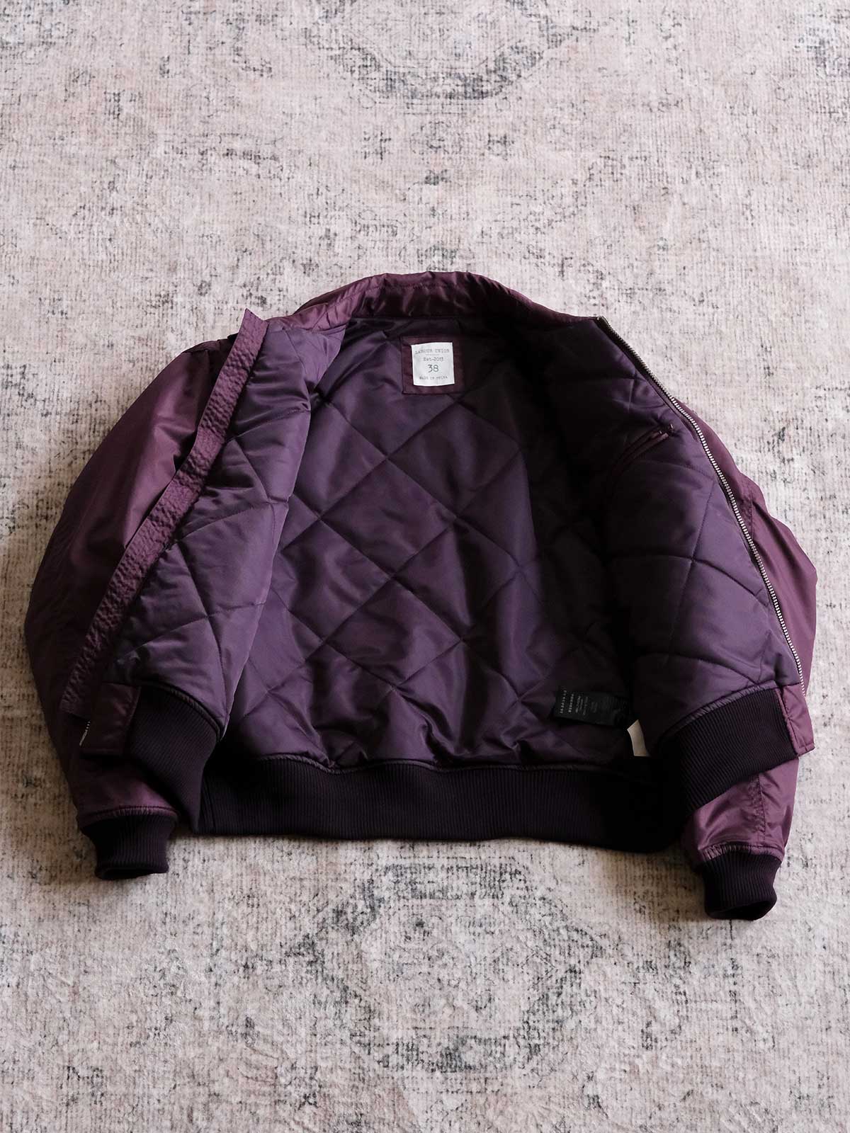 製品画像:
CWU-45Pフライトジャケットの全体展示。高密度ナイロン外層と厚手のキルティング綿を使用した、保温性と防風性に優れたクラシックなフライトジャケットの全体像。
詳細画像:
TALONメタルジッパーとマジックテープエンブレムのディテール。フラップポケットやリブ編みの袖口、裾など、ミリタリーウェア特有のデザインが強調された画像。