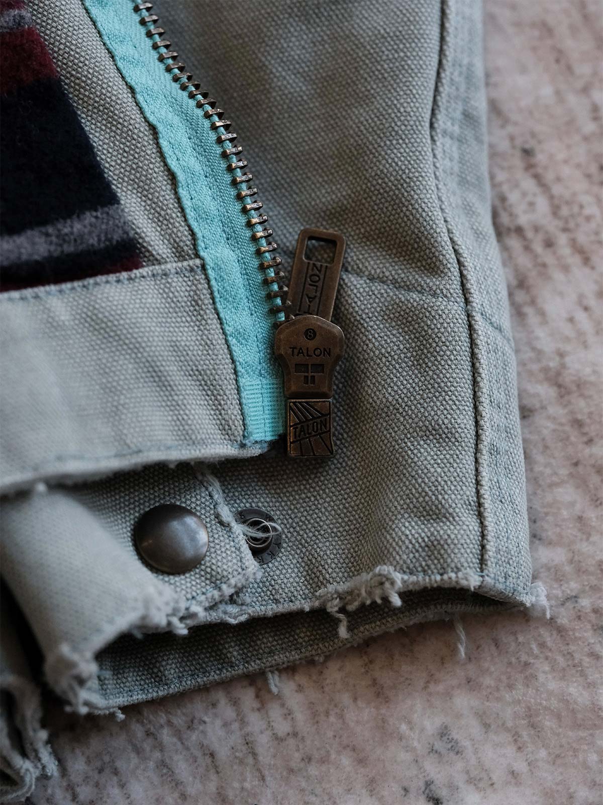 製品画像:
リバイバルダメージパッチワークキャンバスジャケット全体展示。15ozの定織キャンバスと日本製厚ウール裏地を使用し、ヴィンテージスタイルを引き立てるタフなキャンバスジャケットの全体像。
詳細画像:
TALONジッパー、スナップボタン、及び水洗い加工のディテール。多重水洗い加工と手作業のダメージ加工が施された、ヴィンテージ感が強調されたディテール。