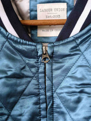 製品画像:
スカジョンスタイル刺繍キルティングジャケット全体展示。1960年代のヨコスカスタイルをインスパイアした、光沢感のあるサテン生地と精緻な刺繍デザインが特徴的なヴィンテージ感溢れるジャケットの全体像。
詳細画像:
精緻な刺繍と光沢サテン生地のディテール。大面積の刺繍デザインと鮮やかな色合いが、ジャケットに強い視覚的インパクトを与えるディテール。