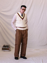 詳細画像:
ツイスト編みの編み目とカラーコンビネーションストライプのディテール。Vネックとストライプデザインが加える視覚的なレイヤード感を強調した画像。
モデル画像:
モデルがシャツと重ね着したVネック クリケットニットベストを着用し、英国風のアカデミックスタイルを演出している画像。