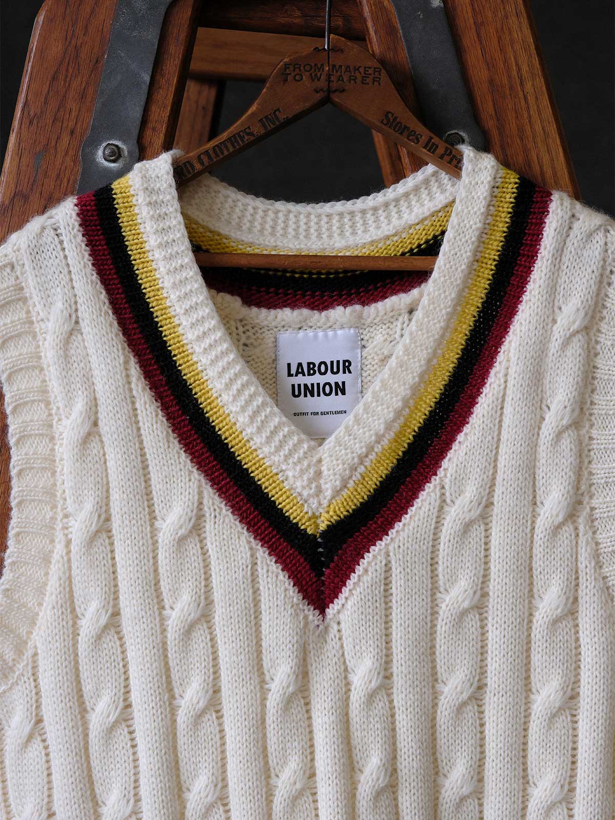 製品画像:
アカデミックスタイルVネック クリケットニットベストの全体展示。クラシックなツイスト編みとストライプデザインが特徴的な、100%ウール素材を使用したVネックデザインのニットベスト。
詳細画像:
ツイスト編みの編み目とカラーコンビネーションストライプのディテール。Vネックとストライプデザインが加える視覚的なレイヤード感を強調した画像。