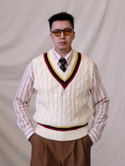 詳細画像:
ツイスト編みの編み目とカラーコンビネーションストライプのディテール。Vネックとストライプデザインが加える視覚的なレイヤード感を強調した画像。
モデル画像:
モデルがシャツと重ね着したVネック クリケットニットベストを着用し、英国風のアカデミックスタイルを演出している画像。