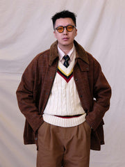 詳細画像:
ツイスト編みの編み目とカラーコンビネーションストライプのディテール。Vネックとストライプデザインが加える視覚的なレイヤード感を強調した画像。
モデル画像:
モデルがシャツと重ね着したVネック クリケットニットベストを着用し、英国風のアカデミックスタイルを演出している画像。