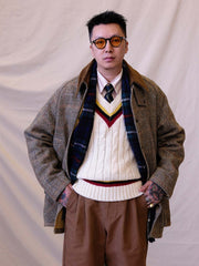 詳細画像:
ツイスト編みの編み目とカラーコンビネーションストライプのディテール。Vネックとストライプデザインが加える視覚的なレイヤード感を強調した画像。
モデル画像:
モデルがシャツと重ね着したVネック クリケットニットベストを着用し、英国風のアカデミックスタイルを演出している画像。