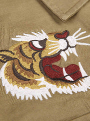 胸元に施されたトラ刺繍と銅製ボタンのディテール特写。蘇繍(ソシュウ)の伝統技法による繊細なステッチと、クラシックなミリタリーグリーンキャンバス素材の質感が特徴