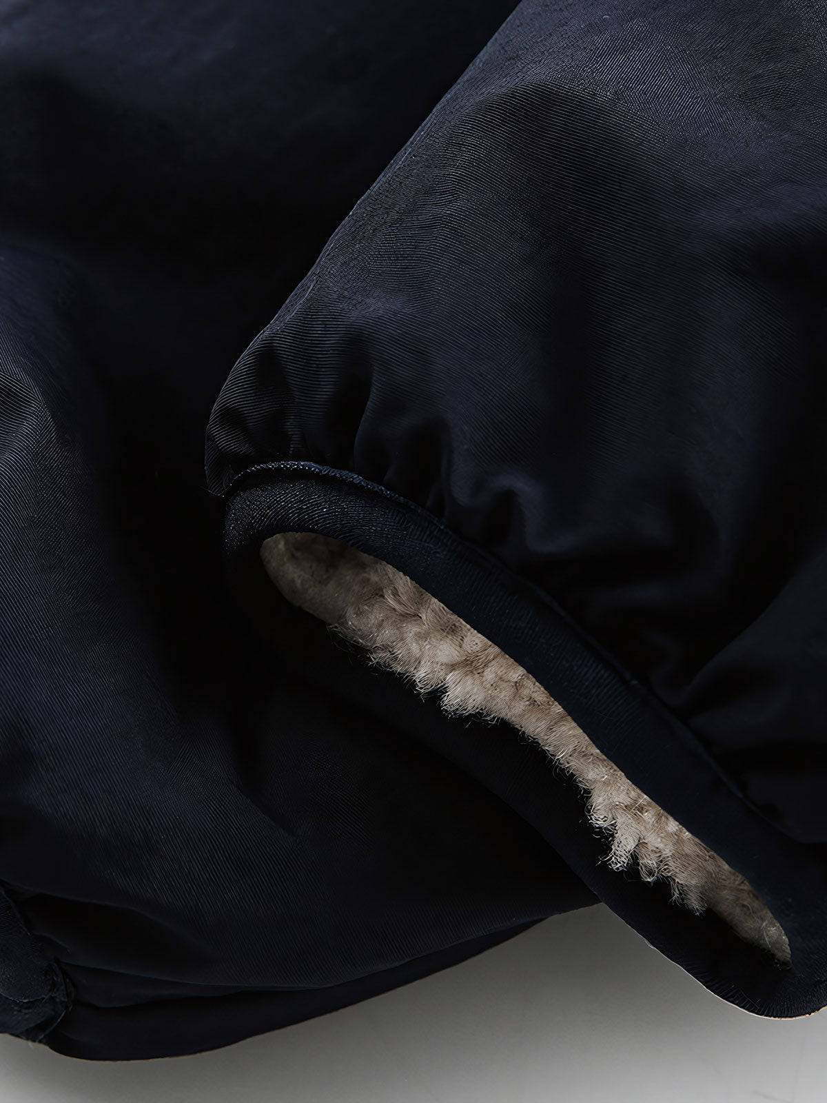 製品画像: リバーシブル シープスキン 中綿ジャケット。柔らかなシープスキンと耐久性のある織りナイロン素材を組み合わせた、多用途デザインの正面全体展示図。
詳細画像: バイカラーデザインと多機能ポケット、さらにハイネック仕様が特徴のリバーシブルジャケットのディテールクローズアップ。